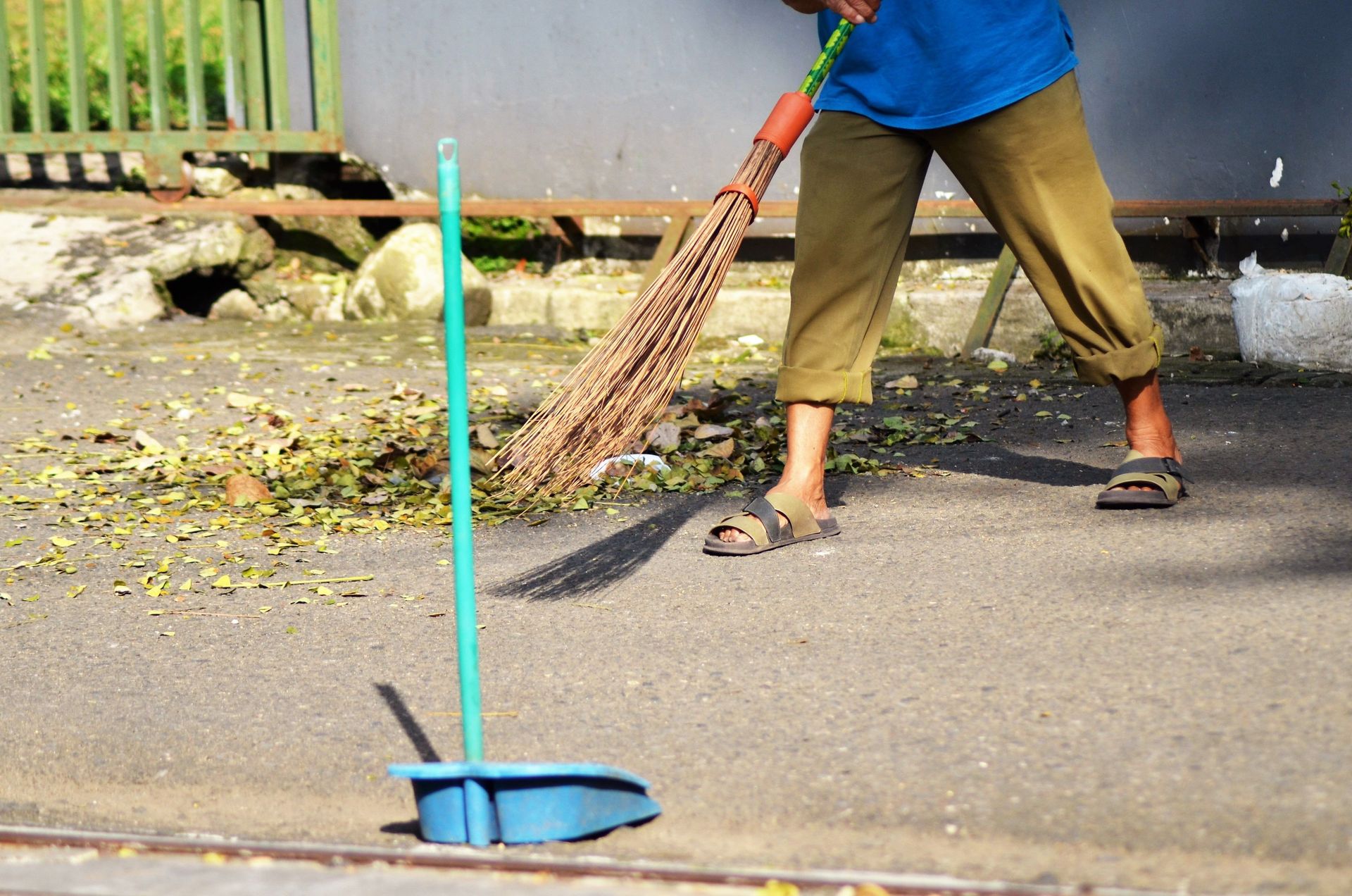 A person engaged in outdoor cleaning, sweeping leaves off the street with a broom and dustpan.